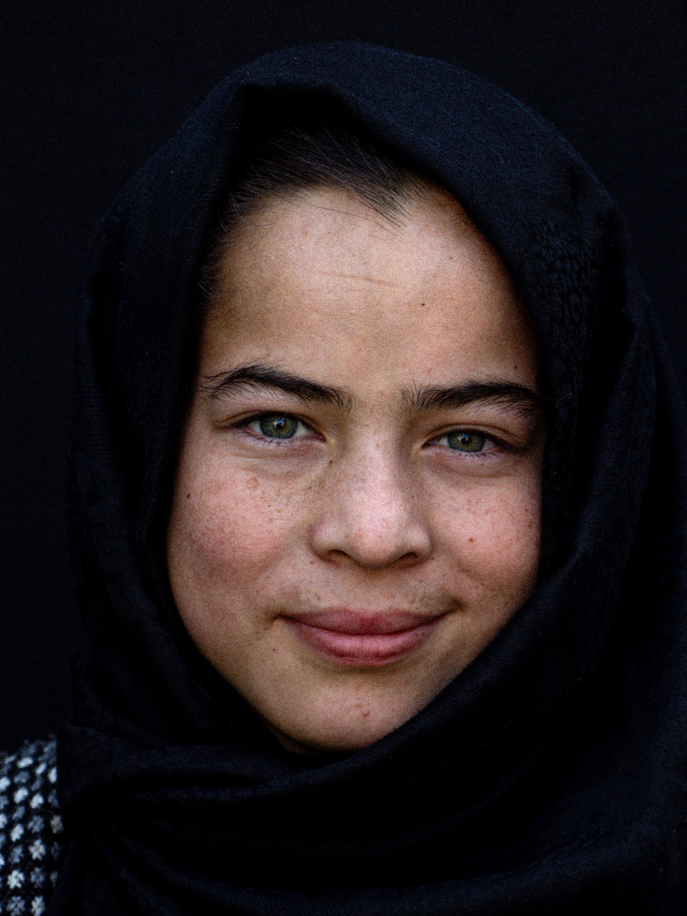 A close-cropped portrait showing a girl in a headscarf with a slight smile on her face.